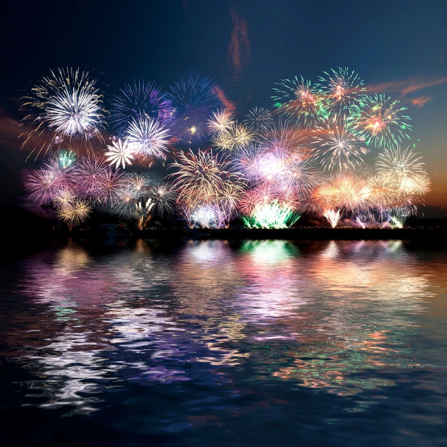 A group of fireworks over the water at night.